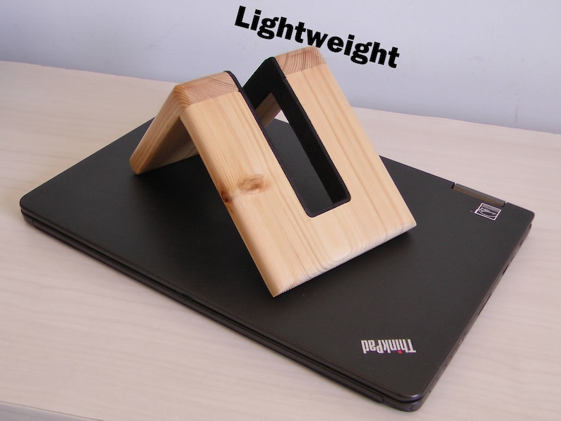 K&ouml;nnte beinhalten: Ein Laptop-St&auml;nder aus Holz mit einem schwarzen Einsatz. Der St&auml;nder ist leicht und hat ein schlichtes Design. Der St&auml;nder steht auf einem schwarzen Laptop mit dem Schriftzug "ThinkPad" auf der Unterseite.