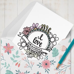 May include: A white card with a black and white floral wreath design. The wreath surrounds a circle with the text "I love Grandma".