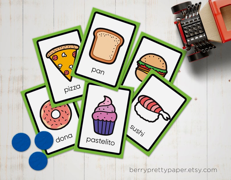 May include: Green flash cards with illustrations of different foods and their names in English and Spanish. The foods include pizza, donut, bread, cupcake, sushi, and a hamburger.