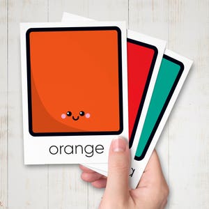 May include: Three cards with a square shape and a happy face on each. The first card is orange and says "orange" at the bottom. The second card is red and the third card is teal.