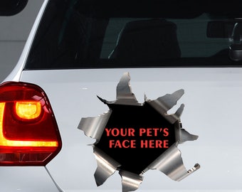 May include: A silver car decal with a torn metal effect, revealing a black space with the text "YOUR PET'S FACE HERE" in red. The decal is applied to the rear of a white car, near the taillight.