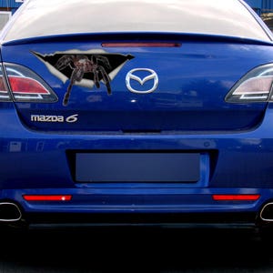 May include: A blue Mazda 6 car with a spider decal on the back. The decal shows a spider crawling out of a hole in the car's body.