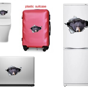 May include: A black bear peeking out of a torn hole on a variety of surfaces, including a toilet, a red suitcase, a laptop, and a white refrigerator.  The bear's face is visible, and the background is white.