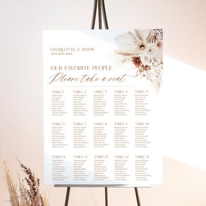 Pode incluir: Um cartão de lugar de casamento branco com um design floral no canto superior direito. O cartão lista as mesas de 1 a 15 com os nomes dos convidados para cada mesa. O texto no topo diz "Charlotte & Jason 27 de junho de 202X" e "Nossas pessoas favoritas Por favor, sentem-se."