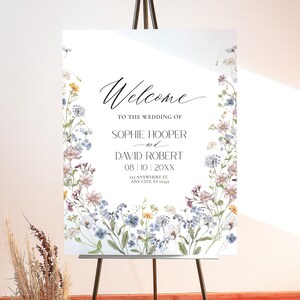 May include: A white welcome sign with a floral border. The text reads "Welcome to the wedding of Sophie Hooper and David Robert 08|10|20XX 123 Anywhere St, Any City, ST 12345".