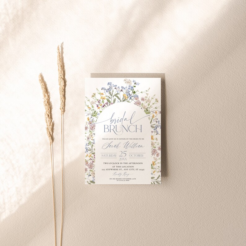 Pu&ograve; includere: Un invito floreale per un brunch nuziale con le parole "bridal BRUNCH" in elegante scrittura. L'invito include il nome "Sarah William", la data, l'ora e il luogo. Il design presenta un arco floreale con fiori colorati.