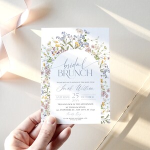 Pu&ograve; includere: Un invito per un brunch nuziale con accenti floreali. L'invito presenta il testo "bridal BRUNCH" e i dettagli dell'evento. Il design include un arco floreale con fiori delicati.