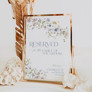 May include: A white wedding sign with a gold frame and floral border. The sign reads "RESERVED for the FAMILY OF THE GROOM thank you! CHARLOTTE & JASON 27TH JUNE 20XX".
