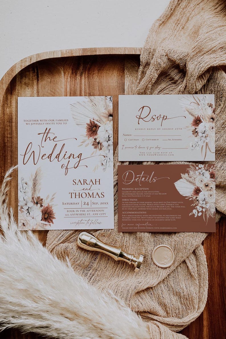 May include: A wedding invitation suite featuring a main invitation, an RSVP card, and a details card, all decorated with dried floral illustrations in white, cream, and rust tones. A gold wax seal stamp and a circular wax seal are included.