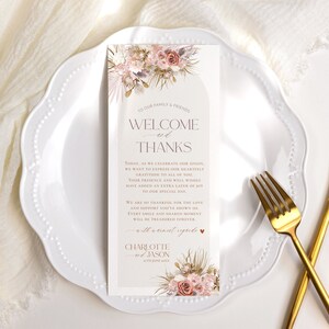 May include: A wedding welcome and thank you sign with a floral design in shades of pink, brown, and beige. The text reads "To our family & friends, Welcome and Thanks." The sign also includes the date "27th June XXXX" and the names "Charlotte and Jason".