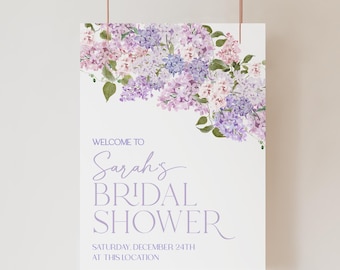 May include: A white bridal shower welcome sign with purple and pink watercolour flowers. The text reads "Welcome to Sarah's Bridal Shower, Saturday, December 24th at this location."