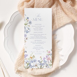 K&ouml;nnte beinhalten: Eine Hochzeitsmen&uuml;karte mit einem floralen Design mit blauen, violetten und rosa Blumen. Das Men&uuml; umfasst Vorspeisen, Hauptgericht, Getr&auml;nke und Desserts. Der Text auf der Karte lautet "The Menu" und "Sarah's Bridal Shower 14.12.20XX".