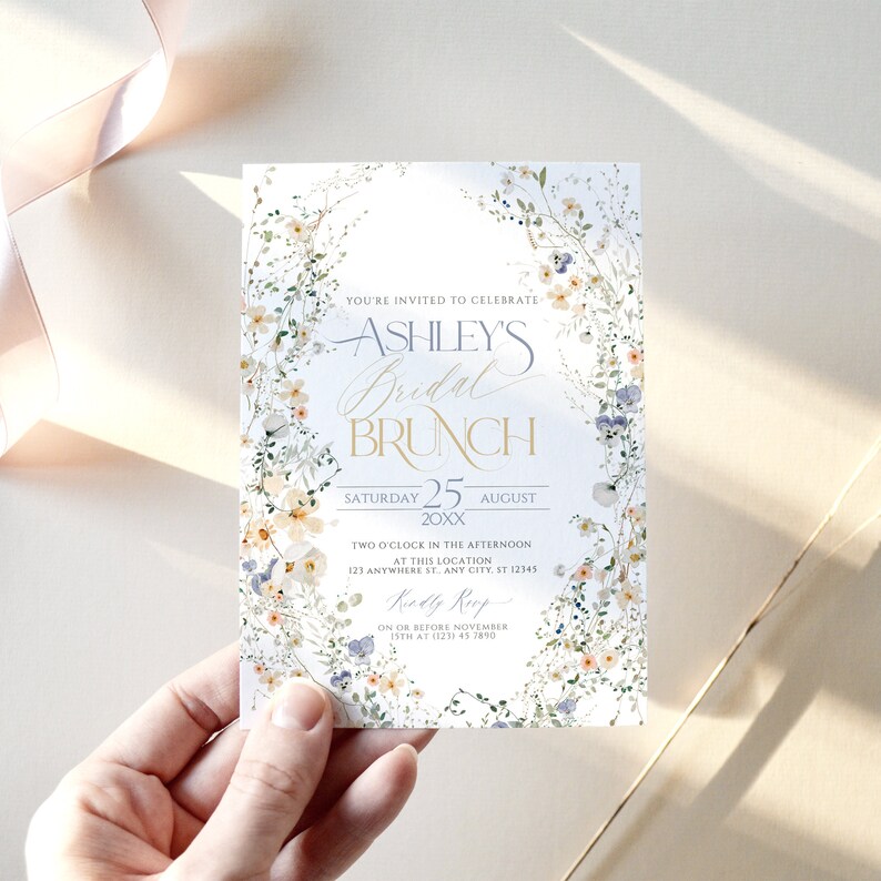 May include: A white floral bridal brunch invitation with gold lettering. The invitation reads "You're invited to celebrate Ashley's Bridal Brunch, Saturday 25 August 20XX, Two o'clock in the afternoon at this location 123 Anywhere St. Any City, ST 12345, RSVP on or before November 15th at (123) 45 7890".