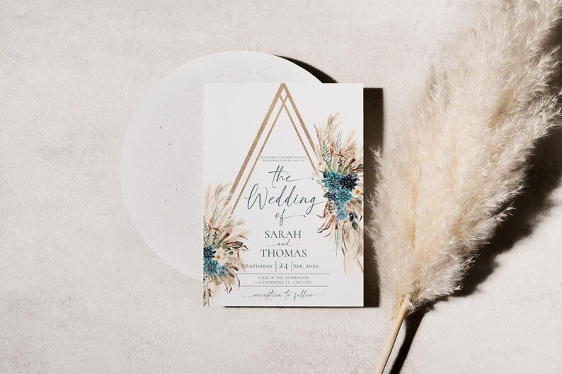 Puede incluir: Una invitaci&oacute;n de boda con un dise&ntilde;o geom&eacute;trico dorado y detalles florales. La invitaci&oacute;n dice "The Wedding of Sarah and Thomas" con la fecha y la hora. Una pluma de hierba de la Pampa beige y esponjosa est&aacute; en el fondo.