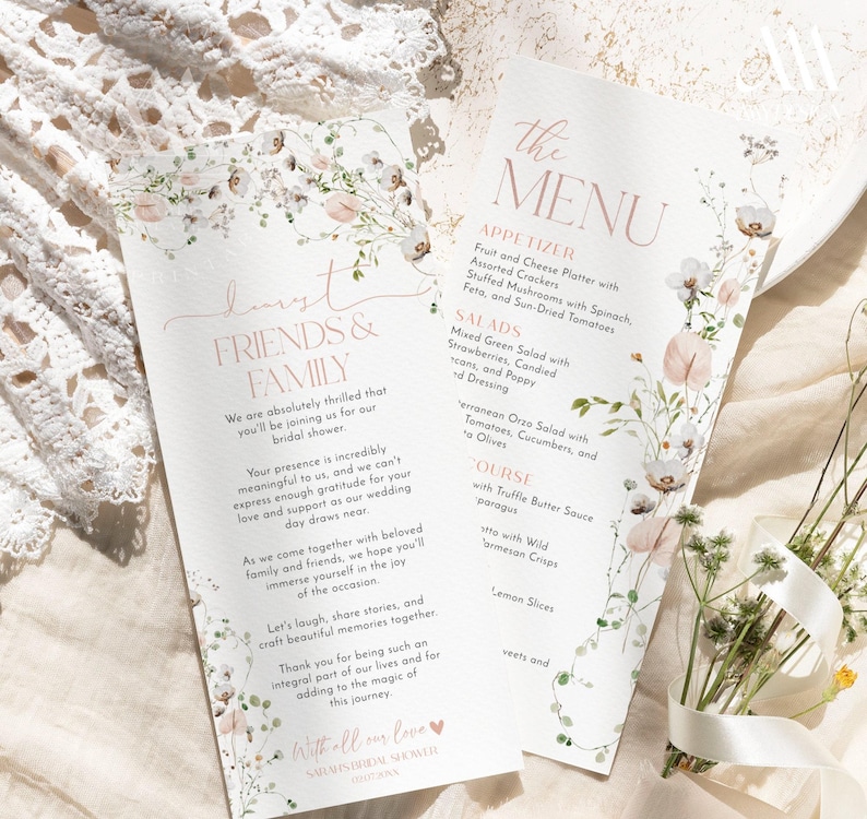 May include: Two white paper cards featuring floral illustrations in soft pink and green tones. One card is titled Dearest Friends & Family, and the other is titled The Menu, listing appetizers, salads, and main courses in elegant typography.