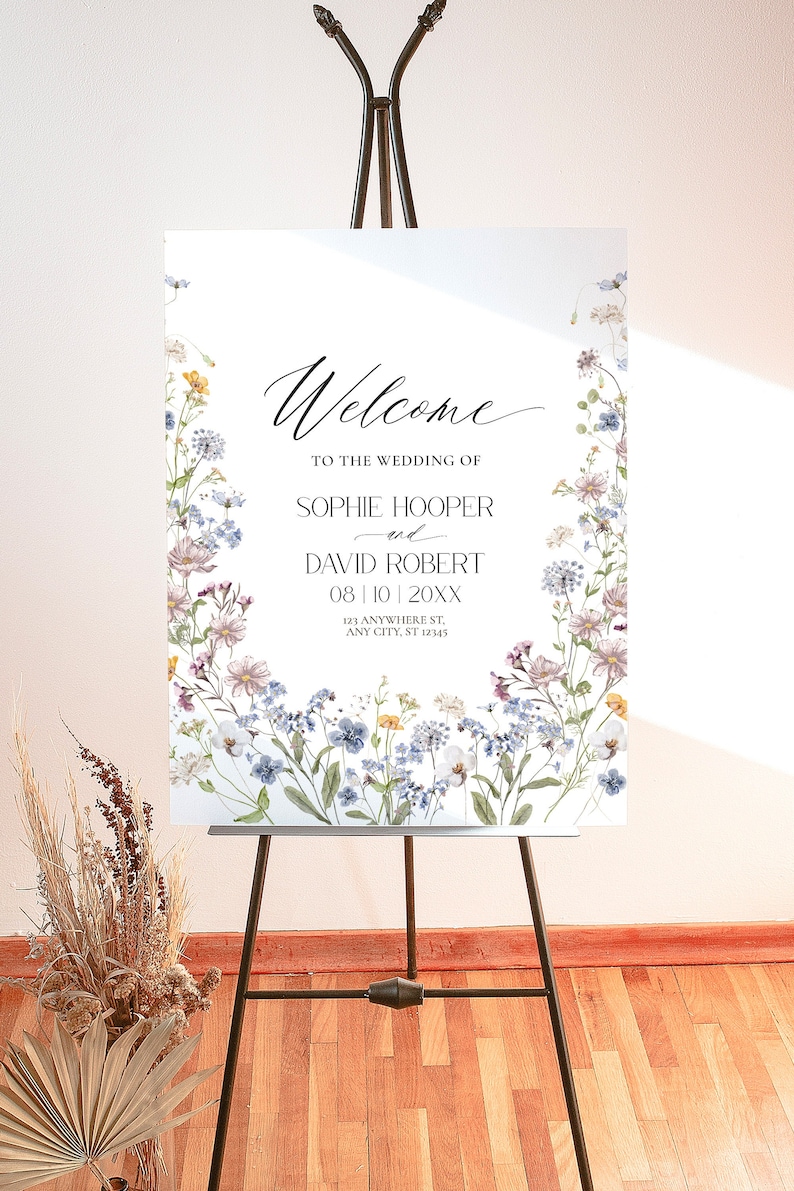 May include: A white welcome sign with a floral border. The text reads "Welcome to the wedding of Sophie Hooper and David Robert 08|10|20XX 123 Anywhere St, Any City, ST 12345".