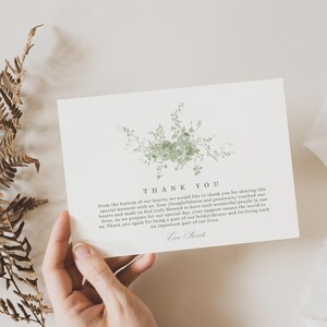 May include: A cream-colored thank you card with a green floral design. The card has the words "THANK YOU" at the top, with a message below. The card is held by a person.