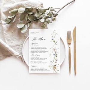 May include: A white wedding menu card with a floral design featuring white and blue flowers. The menu is titled "The Menu" and lists appetizers, main courses, and desserts.