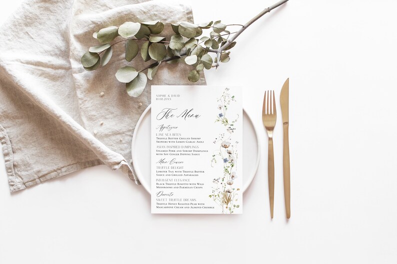 May include: A white wedding menu card with a floral design featuring white and blue flowers. The menu is titled "The Menu" and lists appetizers, main courses, and desserts.
