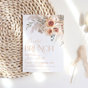 May include: A rectangular invitation card featuring a floral arrangement of pampas grass and roses in shades of peach and cream. The text reads Bridal BRUNCH, Julia Smith, Sunday 25th February 20XX, and includes RSVP details.