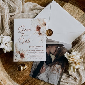 May include: A Save the Date card featuring floral illustrations, the text Jessica Hooper and Richard Anderson, and a photograph of a couple kissing. The set includes a white envelope sealed with a gold wax stamp and decorative dried flowers.