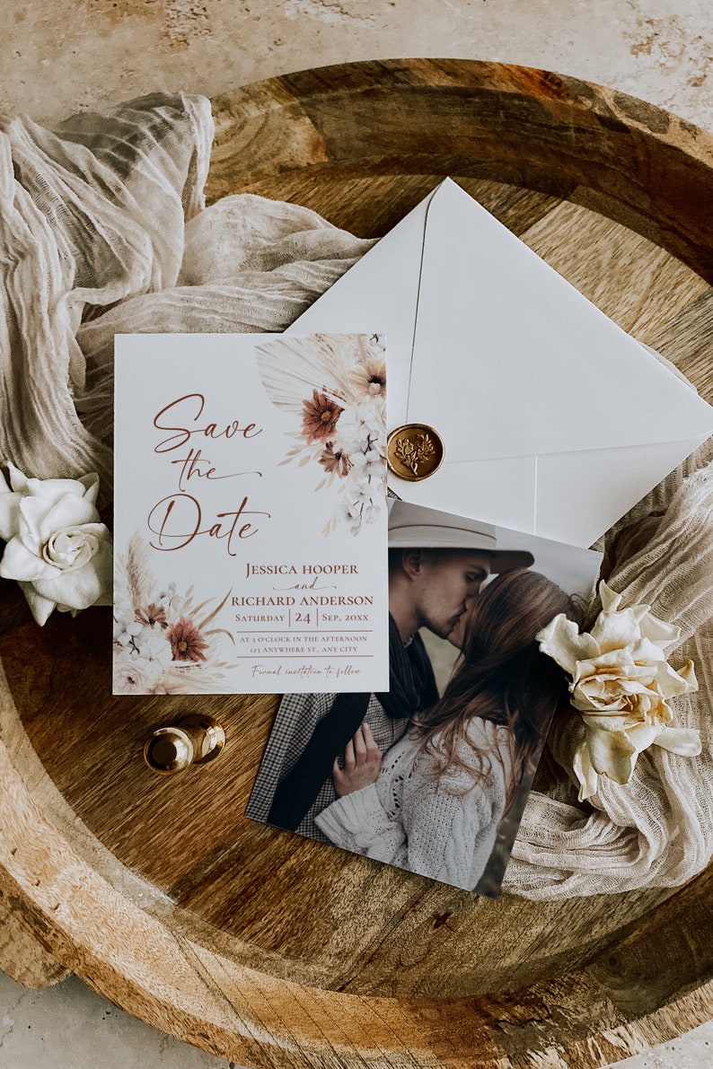 May include: A Save the Date card featuring floral illustrations, the text Jessica Hooper and Richard Anderson, and a photograph of a couple kissing. The set includes a white envelope sealed with a gold wax stamp and decorative dried flowers.