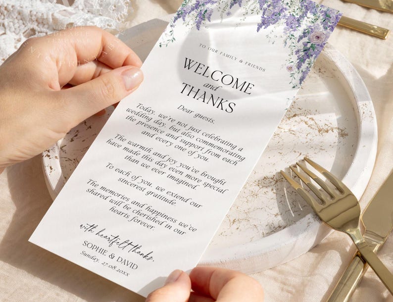 May include: A rectangular white wedding welcome card featuring a purple floral illustration at the top. The text reads: TO OUR FAMILY & FRIENDS, WELCOME and THANKS, Dear guests, followed by a message, with heartfelt thanks, SOPHIE & DAVID, 27.08.20xx.