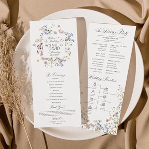 May include: A wedding ceremony program with a floral design featuring blue and purple flowers. The program includes the wedding party, ceremony order, and wedding timeline. The text reads "Welcome to the Wedding of Sophie & David Saturday 08.07.20XX".