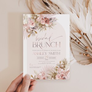 May include: A blush pink and white floral bridal brunch invitation with a gold and white RSVP card. The invitation features the text "bridal brunch" and "Ashley Smith" with a date of December 25th.