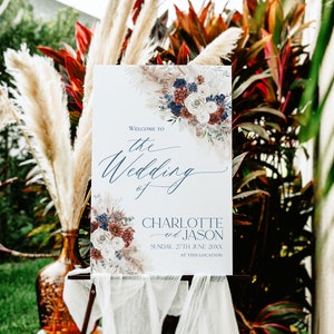 May include: A wedding welcome sign featuring a watercolour floral design in shades of blue, white, and red. The sign reads "Welcome to the Wedding of Charlotte and Jason, Sunday, 27th June 20XX, at this location."