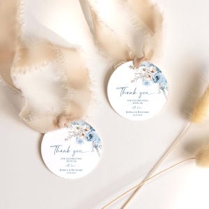 Pu&ograve; includere: Due etichette regalo rotonde bianche con un'illustrazione floreale blu ad acquerello nella parte superiore. Il testo recita Thank you FOR CELEBRATING WITH US with love JESSICA & RICHARD 09.25.20XX. Ogni etichetta &egrave; fissata a un nastro di seta beige sfilacciato.