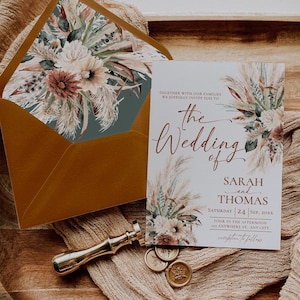May include: A wedding invitation card and matching envelope featuring a floral and pampas grass design. The card text reads: Together with our families we joyfully invite you to the Wedding of Sarah and Thomas, Saturday 24 Sep, 20XX.