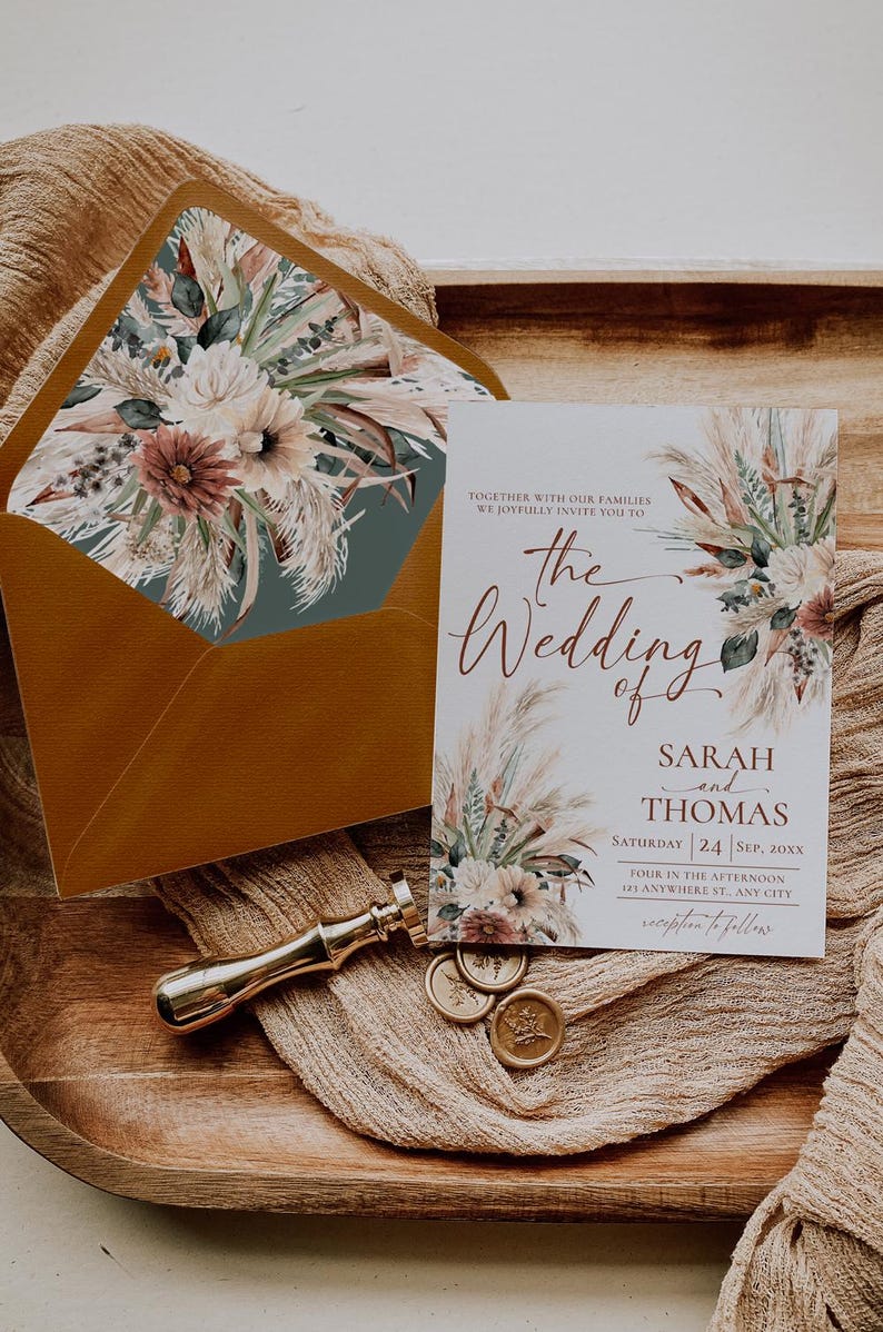 May include: A wedding invitation card and matching envelope featuring a floral and pampas grass design. The card text reads: Together with our families we joyfully invite you to the Wedding of Sarah and Thomas, Saturday 24 Sep, 20XX.