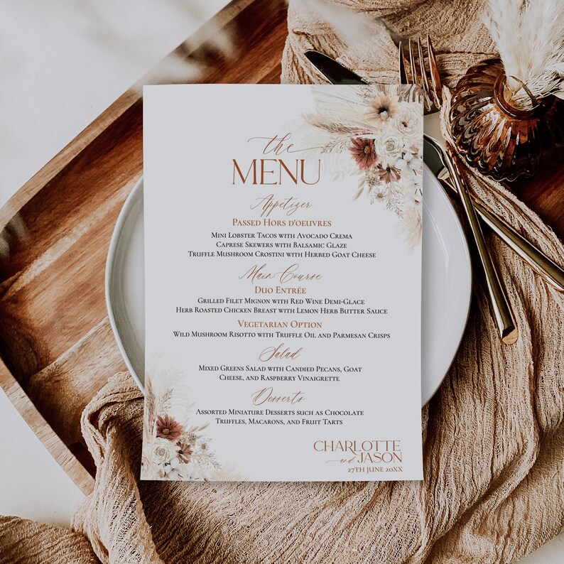 May include: A rectangular wedding menu card featuring the text "the MENU" and "CHARLOTTE and JASON 27TH JUNE 20XX" with printed floral illustrations of dried pampas grass, white roses, and rust-colored flowers in the top right and bottom left corners.