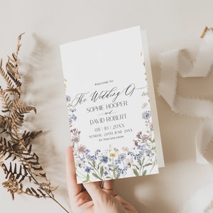May include: A wedding ceremony order of service card with a floral design featuring blue, purple, and white flowers. The text reads "Welcome to The Wedding of Sophie Hooper and David Robert 08/10/20XX Sunday, 24th June 20XX At This Location."