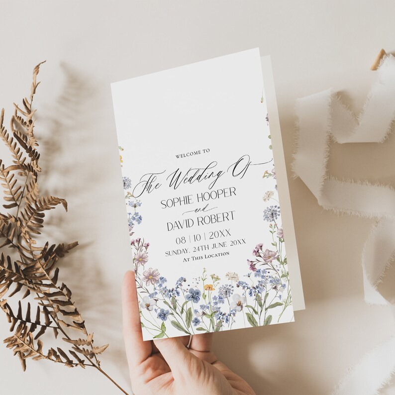 May include: A wedding ceremony order of service card with a floral design featuring blue, purple, and white flowers. The text reads "Welcome to The Wedding of Sophie Hooper and David Robert 08/10/20XX Sunday, 24th June 20XX At This Location."