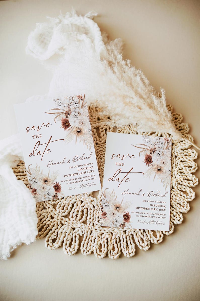 May include: Two save the date cards with a floral design and the text "save the date" in a cursive font. The cards are on a woven placemat with a dried flower arrangement.