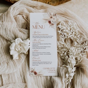 May include: A vertical wedding menu card featuring floral illustrations at the top and bottom. The text lists appetizers, main courses, salad, and desserts, concluding with the names Charlotte and Jason and the date 27th June 20XX.
