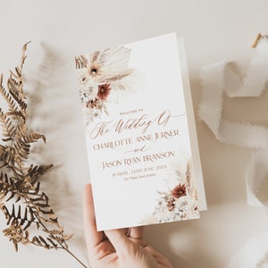 May include: A wedding ceremony order of service with a white background and a floral design featuring dried pampas grass, white and red flowers. The text reads "Welcome to The Wedding of Charlotte Anne Jurner and Jason Ryan Branson, Sunday, 24th June 20XX, At This Location."