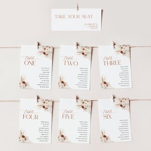 Puede incluir: Un conjunto de tarjetas de mesa de boda y un letrero. El letrero dice "TAKE YOUR SEAT" encima de los nombres "CHARLOTTE y JASON". Las tarjetas de mesa est&aacute;n numeradas del uno al seis, con nombres de invitados y detalles florales. Las tarjetas son blancas con texto marr&oacute;n.