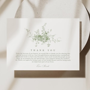 May include: A white card with a green floral design and the words "THANK YOU" at the top. Below the text is a message of gratitude. The card is on a light-colored, textured surface.