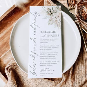 May include: A rectangular white wedding thank you card featuring a floral illustration of pampas grass and dried leaves at the top. The text reads: Beloved friends and family, Welcome and Thanks, We are deeply grateful for your presence on our special day. Sophie & David 10.08.20XX.