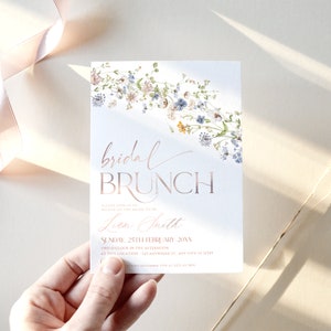 May include: A white invitation card with a floral design in shades of blue and pink. The text "bridal brunch" is written in rose gold lettering. The invitation is for a bridal brunch for Lian Smith on Sunday, 25th February at 2:00 PM. The location is 123 Anywhere St., Any City, ST 12345.