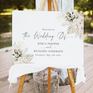 May include: A rectangular white wedding sign on a wooden easel featuring floral illustrations in beige, cream, and green. The text reads: Welcome To the Wedding Of JESICA HOOPER and RICHARD ANDERSON Saturday | 24 | Sep, 20XX.
