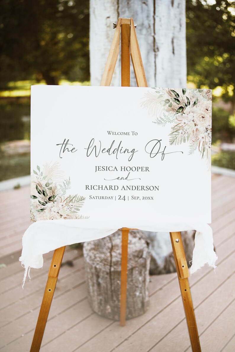 May include: A rectangular white wedding sign on a wooden easel featuring floral illustrations in beige, cream, and green. The text reads: Welcome To the Wedding Of JESICA HOOPER and RICHARD ANDERSON Saturday | 24 | Sep, 20XX.