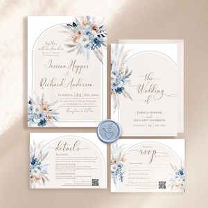 May include: A wedding invitation suite featuring a main invitation, details card, RSVP card, and envelope, all adorned with watercolor blue and beige floral arrangements and pampas grass. A light blue wax seal sits between the cards.