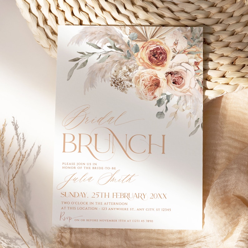 May include: A white invitation card featuring a floral arrangement of pampas grass and roses in shades of peach and cream. The text reads Bridal BRUNCH, Julia Smith, Sunday, 25th February 20XX, two o'clock, and RSVP details.