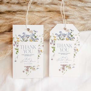 May include: Two white thank you tags with a floral design featuring blue and yellow flowers. The text on the tags reads "Thank You for making today so special!" and includes the text "Sarah's Bridal Shower 12.12.20XX".