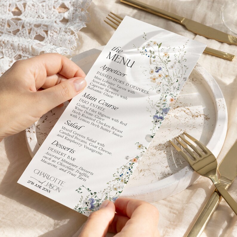 Puede incluir: Una tarjeta de men&uacute; blanca con un dise&ntilde;o floral. El men&uacute; incluye aperitivos, platos principales, ensalada y postres. El texto en la tarjeta de men&uacute; dice "the MENU", "Appetizer", "PASSED HORS D'OEUVRES", "Mini Lobster Tacos with Avocado Crema", "Caprese Skewers with Balsamic Glaze", "Main Course", "DUO ENTR&Eacute;E", "Grilled Filet Mignon with Red Wine Demi-Glace", "Herb Roasted Chicken Breast with Lemon Herb Butter Sauce", "Salad", "Mixed Greens Salad with Candied Pecans, Goat Cheese, and Raspberry Vinaigrette", "Desserts", "DESSERT BAR", "Assorted Miniature Desserts such as Chocolate Truffles, Macarons, and Fruit Tarts", "CHARLOTTE", "JASON", "27TH JUNE 20XX".