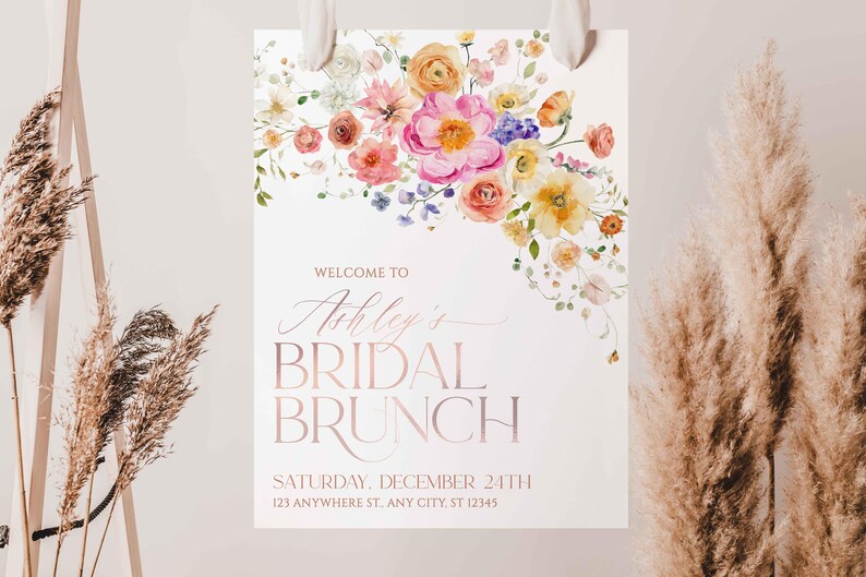 May include: A white rectangular sign featuring a watercolor floral arrangement in shades of pink, yellow, and orange at the top. The text reads: WELCOME TO Ashley's BRIDAL BRUNCH SATURDAY, DECEMBER 24TH 123 ANYWHERE ST, ANY CITY, ST 12345.